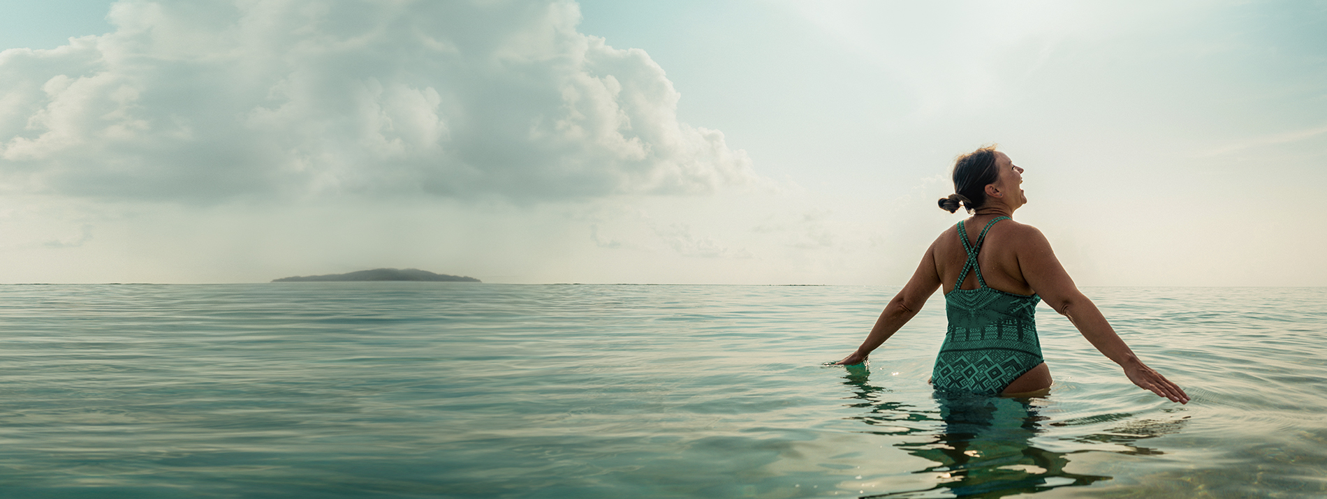  Frau im Badeanzug steht mit den Armen ausgebreitet im Meer/Wasser